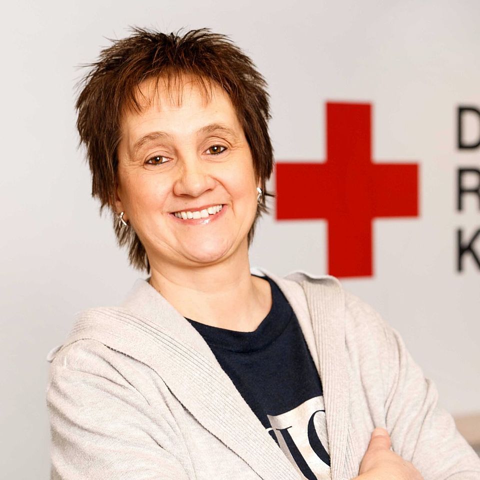 Mitarbeiterin Kreisgeschäftsstelle Buchhaltung, dunkles kurzes Haar, freundlich lächelnd im Hintergrund eine weisse Wand mit roten Kreuz Logo